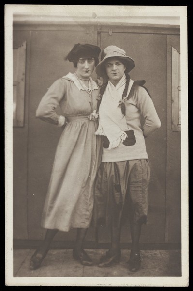 Download the full-sized image of Two men, both in drag, pose wearing hats and make-up. Photographic postcard, ca. 1918.