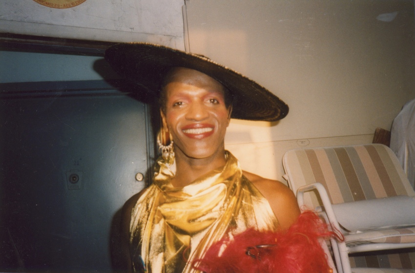 Download the full-sized image of A Photograph of Marsha P. Johnson Wearing a Black Hat and a Gold Dress