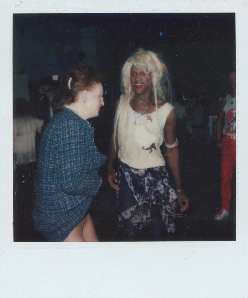 Download the full-sized image of A Photograph of Marsha P. Johnson with Blonde Hair, White Top, and Black and Pink Patterned Skirt, Dancing with Another Person