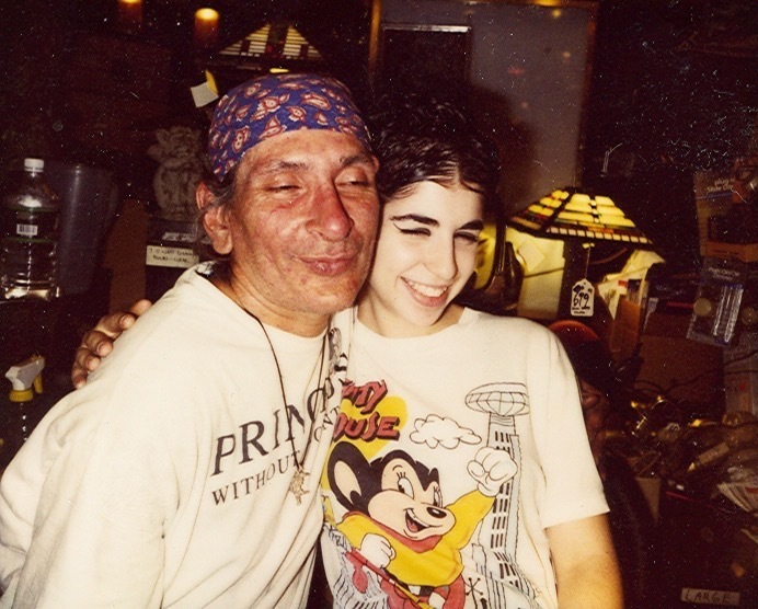 Download the full-sized image of A Photograph of Sylvia Rivera Hugging Another Person Wearing a White T-Shirt and a Bandana at Uplift Lighting