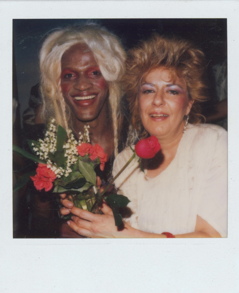 Download the full-sized image of A Photograph of Marsha P. Johnson With Blonde Hair and Red Eyeshadow, Smiling with an Unknown Person Holding a Flower Bouquet