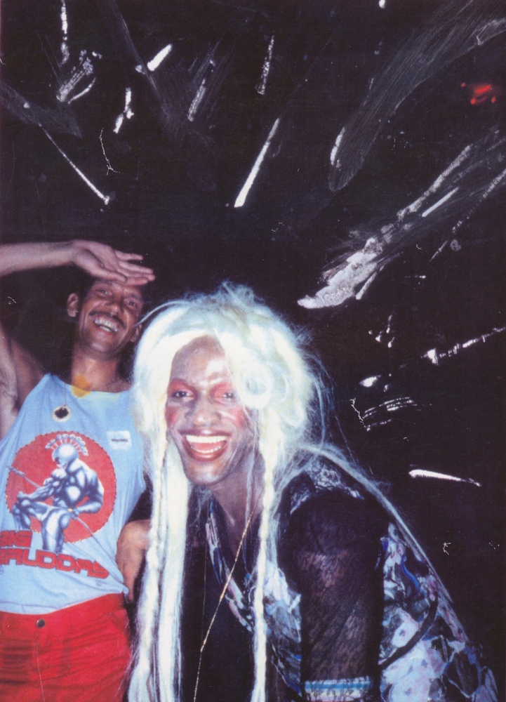 Download the full-sized image of A Photograph of Marsha P. Johnson Leaning Forward and Laughing with Blonde Hair and a Black and Pink Patterned Dress
