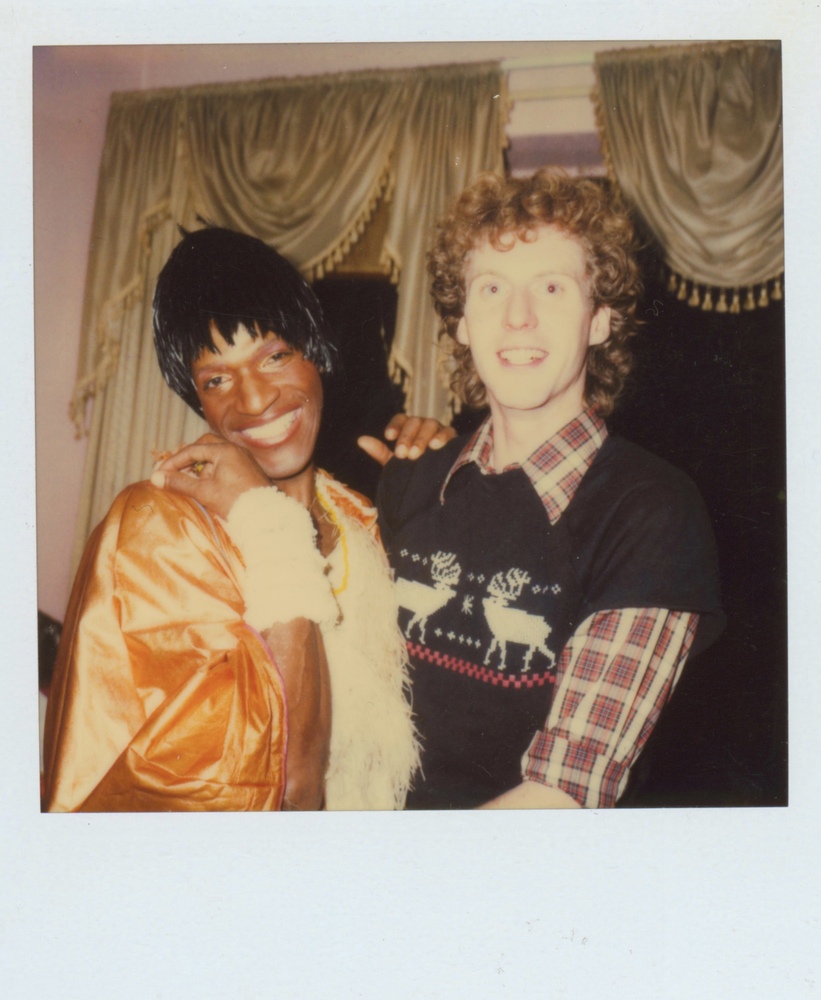 Download the full-sized image of A Photograph of Marsha P. Johnson Wearing a White and Orange Dress While Posing with Her Hand on George Flimlin’s Shoulder