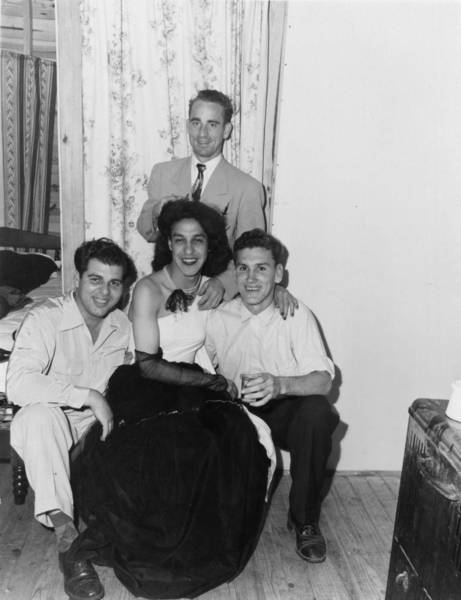 Download the full-sized image of Person in Black and White Gown Sits Surrounded by Three Others