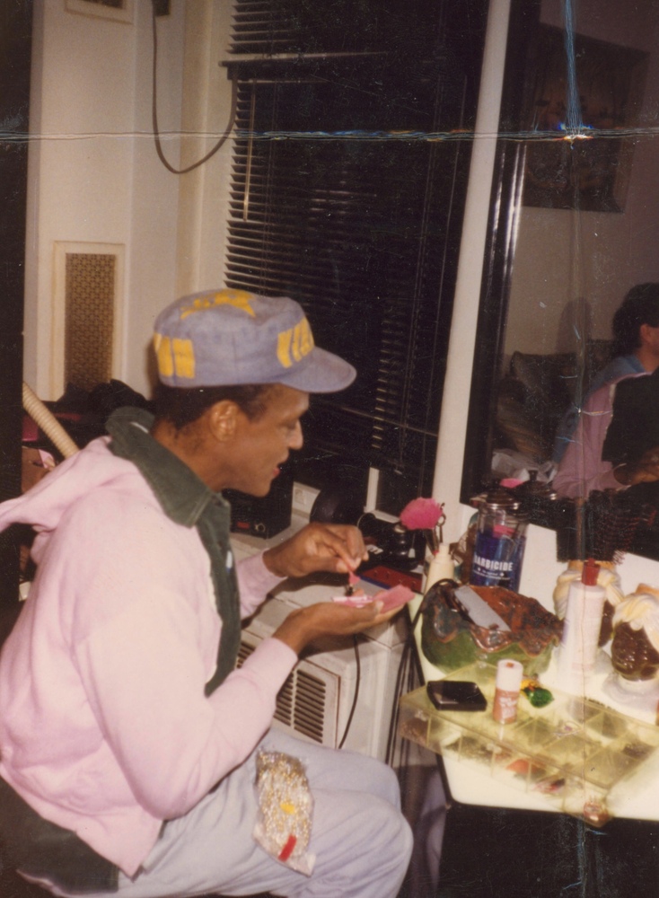 Download the full-sized image of A Photograph of Marsha P. Johnson Sitting at a Side Table Applying her Makeup