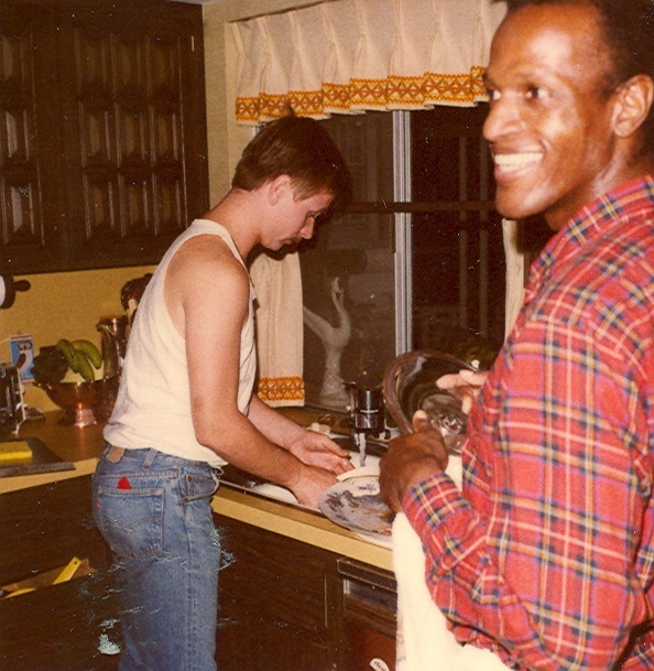 Download the full-sized image of A Photograph of Marsha P. Johnson Wearing a Red Flannel Shirt While Washing the Dishes