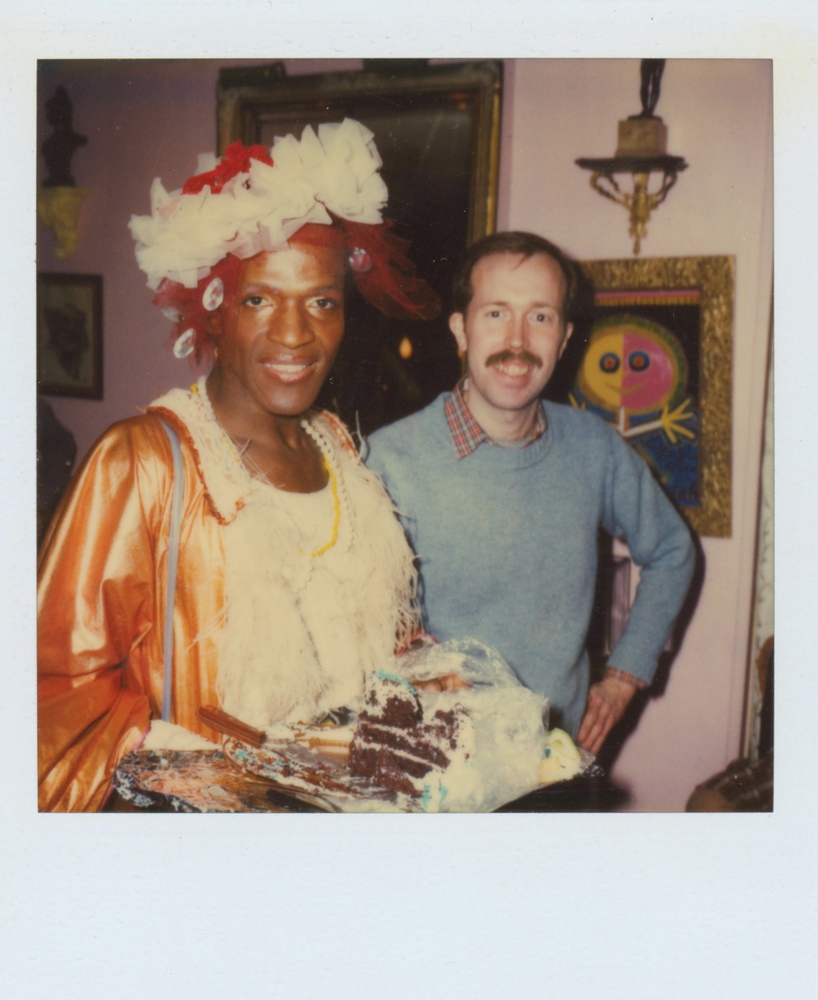 Download the full-sized image of A Photograph of Marsha P. Johnson Wearing a White and Orange Dress While Holding a Cake