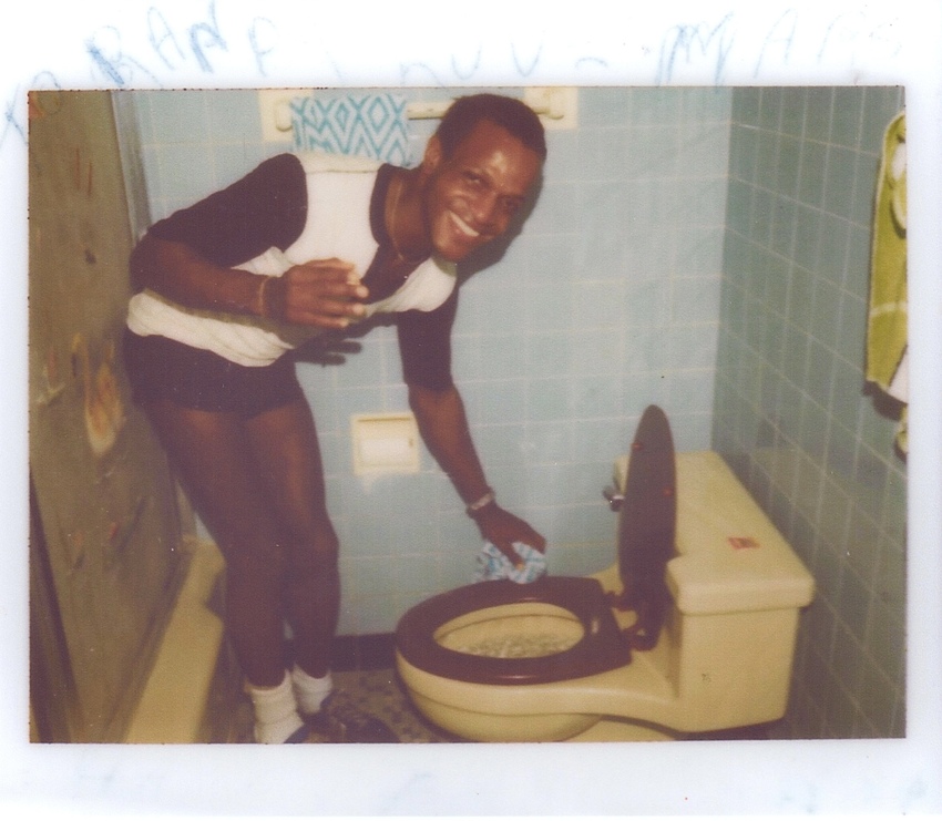 Download the full-sized image of A Photograph of Marsha P. Johnson Cleaning a Toilet and Smiling at the Camera