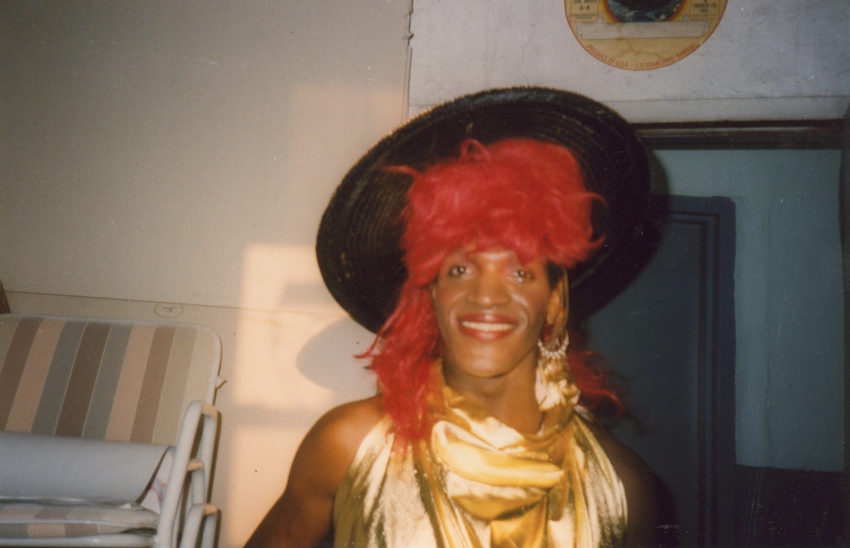Download the full-sized image of A Photograph of Marsha P. Johnson Wearing a Black, Red, and Gold Outfit
