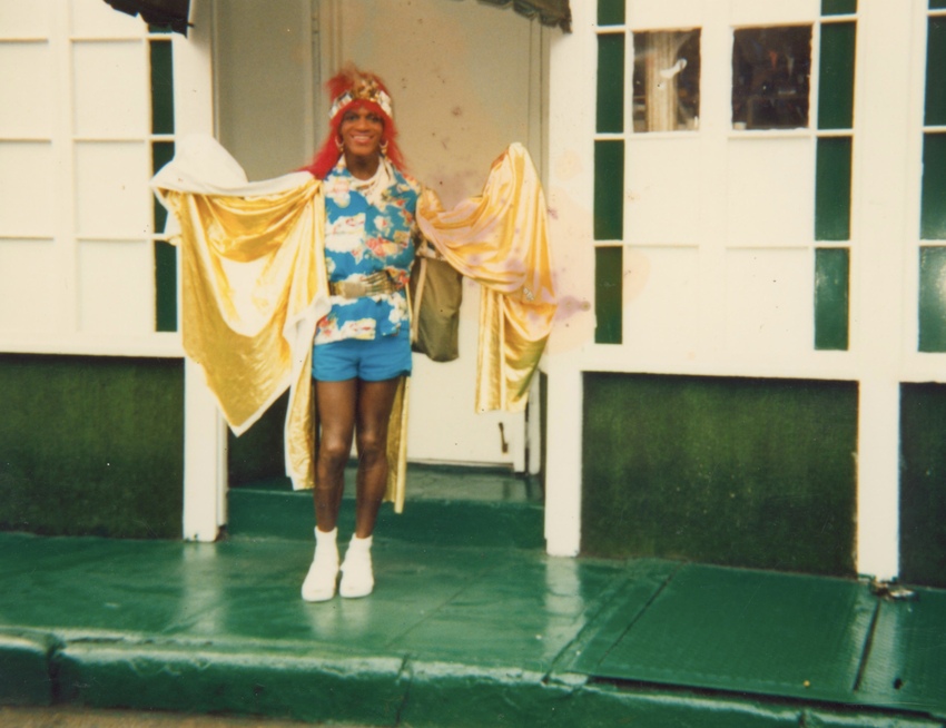 Download the full-sized image of A Photograph of Marsha P. Johnson with Red Hair, Wearing a Blue Hawaiian Shirt and Draped in Yellow Fabric