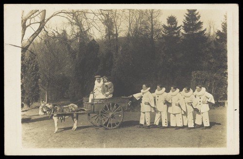 Download the full-sized image of Soldiers, one in drag, with a donkey and cart, posing on the grass in front of trees. Photographic postcard, 191-.