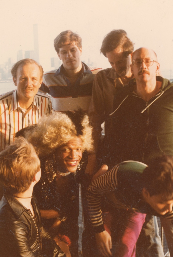 Download the full-sized image of A Photograph of Marsha P. Johnson With Curly Blonde Hair, Leaning Forward Posing Outside with Friends