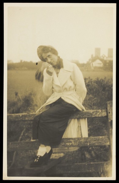 Download the full-sized image of An actor in drag, posing on a stile in a field. Photographic postcard, ca. 1920.