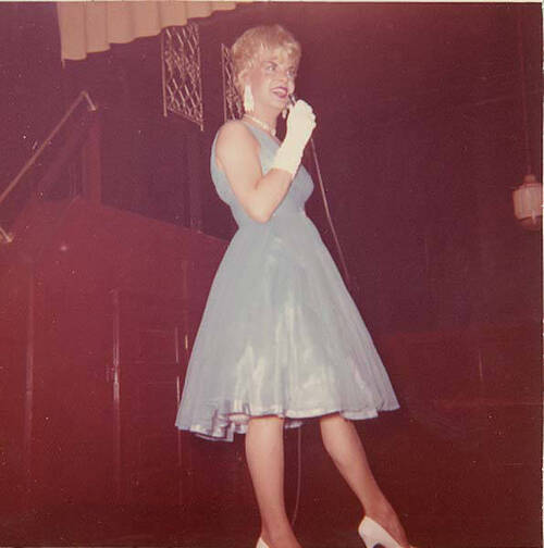 Download the full-sized image of Female impersonator in light blue midi dress on stage with microphone